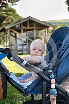 Cute baby in a stroller looking to the side curiously in a sunny park in Rattvik, Sweden photo
