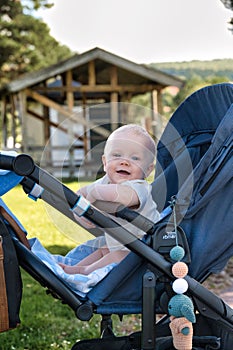 Cute baby in a stroller smiling happily at the camera in a sunny park in Rattvik, Sweden photo