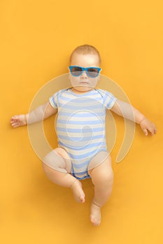 Cute baby with sunglasses lying on an orange dress wearing baby sailor suit with blue and white stripes and enjoying sunbathing