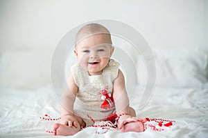 Cute baby toddler boy, playing with white and red bracelets