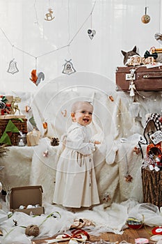 Cute baby toddler girl near the Christmas tree with toys and garlands at home. Cute little baby girl with christmas toys