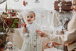Cute baby toddler girl near the Christmas tree with toys and garlands at home. Cute little baby girl with christmas toys