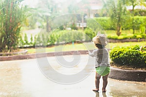 Cute baby toddler girl standing outdoors under the rain with bare feet. Kid is enjoying the warm summer rain. Childhood