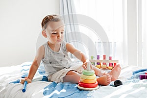 Cute baby toddler playing with learning toy pyramid stacking blocks at home. Early age Montessori education. Kids hand brain fun