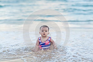 Cute baby wearing a blue striped cartoon swimsuit sitting and playing on the beach near the sea