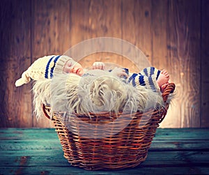 Cute baby wearing knitted funny costume, sleeping in a basket over wooden background