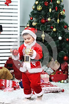 Cute baby wearing a red santa claus costume on a couch at home in christmas