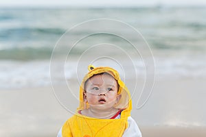 Cute baby wearing a yellow cartoon bathrobe sitting and playing on the beach near the sea