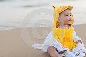 Cute baby wearing a yellow cartoon bathrobe sitting and playing on the beach near the sea