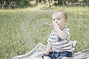 Cute bady boy with big beautiful eyes sitting on grass outdoor on nature