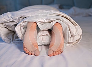 cute bare feet of a child wrapped in a blanket on the bed close-up