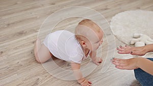 Cute barefoot baby infant girl is crawling on wooden floor in living room at home, smiling and change emotion. Concept
