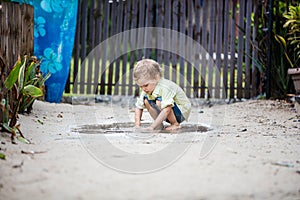 Cute barefoot boy plunging hands in puddle