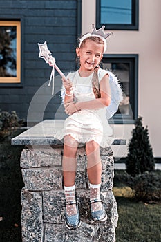 Cute beaming girl wearing fairy wings and holding magic wand having fun