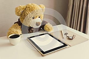 Cute bear doll watching taplet on table