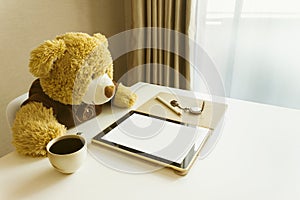 Cute bear doll watching taplet on table