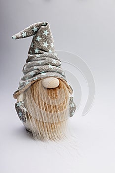 Cute bearded gnome in a cap with stars on a light background. Handmade soft toy. Home decor. Vertical shot. Copy space