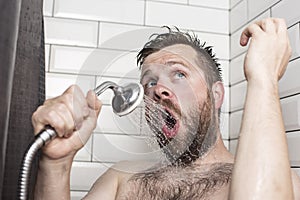 Cute bearded man singing in the bathroom using the shower head with flowing water instead of a microphone