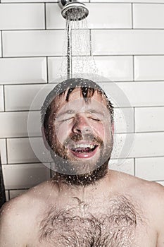 Cute bearded man standing in the shower under running water and