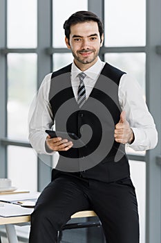 Cute and beautiful Asian businessman sitting in office and holding a tablet computer and rise hand for thumbs up with self-