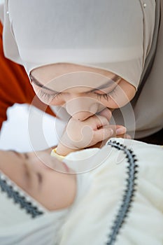 A cute and beautiful Asian Muslim in hijab dress kissing her baby daughter with a tender gesture. Love, care, and relationship