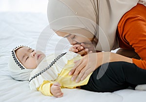 A cute and beautiful Asian Muslim in hijab dress kissing her baby daughter with a tender gesture. Love, care, and relationship