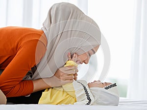 A cute and beautiful Asian Muslim in hijab dress kissing her baby daughter with a tender gesture. Love, care, and relationship