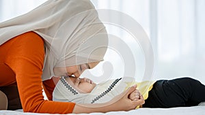 A cute and beautiful Asian Muslim in hijab dress kissing her baby daughter with a tender gesture. Love, care, and relationship