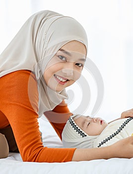 A cute and beautiful Asian Muslim in hijab dress take a look for her baby daughter with a tender gesture. Love, care, and