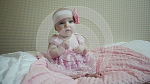 Cute beautiful baby girl sitting on a bed in pink dress