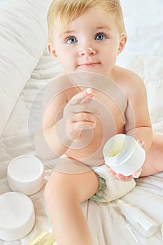 Cute, beautiful child, little baby girl with cream on nose and finger, in diaper in bed at home. Skincare products