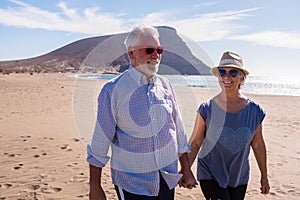 Cute and beautiful couple of seniors having fun together and enjoying their vacations at the beach walking on the sand and smiling