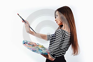 Cute beautiful girl artist holding a palette and brush in the process draws inspiration. White background, isolated.