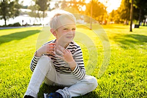 Cute beautiful happy little boy sit on grass enjoying summer time