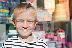 Cute beautiful happy little boy smiling in front of shop-window, looking at camera