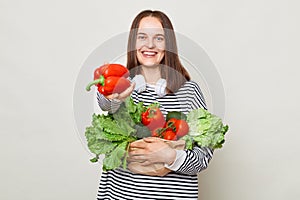 Cute beautiful healthy woman embraces fresh vegetables posing  over white background offering red pepper enjoying orgnic
