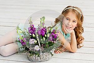 Cute beautiful little girl with blond hair is lying in a bright studio next to a basket with fresh flowers