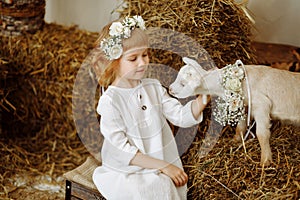 A cute and beautiful little girl is sitting in the hayloft with a goat