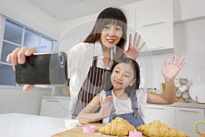 A cute and beautiful mother with young and little daughter, 7 years old, taking a selfie photo with a smartphone in modern kitchen