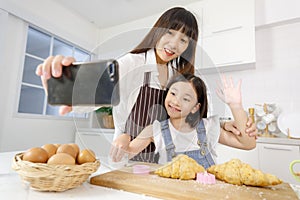 A cute and beautiful mother with young and little daughter, 7 years old, taking a selfie photo with a smartphone in modern kitchen