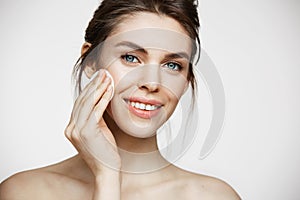 Cute beautiful natural brunette girl cleaning face with cotton sponge smiling looking at camera over white background