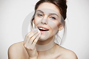 Cute beautiful natural brunette girl cleaning face with cotton sponge smiling looking at camera over white background