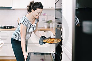 Beautiful pregnant woman in home kitchen preparing pizza and baking