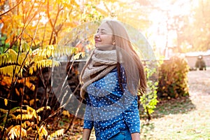 Cute beautiful smile woman walking in red autumn park. Girl in knitten scarf near tree and she is happy