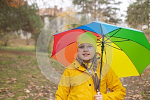 Cute beautiful teenage girl in an orange pants, raincoat and hat with rainbow-colored umbrella. Cosiness, autumn