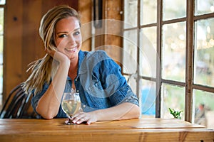 Cute beautiful woman sitting at a local pub bar brewery restaurant next to a window on a bright sunny day