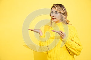 Cute beautiful woman wearing yellow sweater standing over yellow isolated background with convincing face, pointing with hands to photo