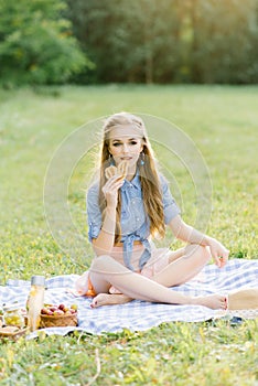 Cute beautiful young and youthful girl with professional makeup sitting on plaid, summer picnic. She eats a croissant