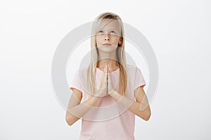 Cute believing female child holding hands in pray and looking up with confident calm expression, praying or asking god