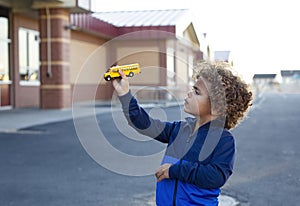 Cute bi-racial schoolboy holding a toy yellow school bus as he plays in an outdoor schoolyard.